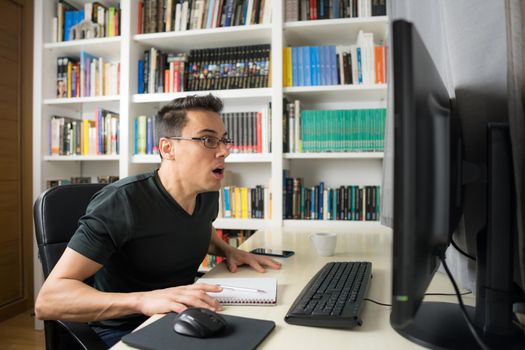 Seated man in black shirt looking at the computer screen very surprised. Mid shot.