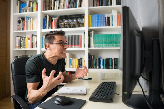 Seated man in a black shirt in front of the computer, hysterical because he does not understand something. Mid shot.