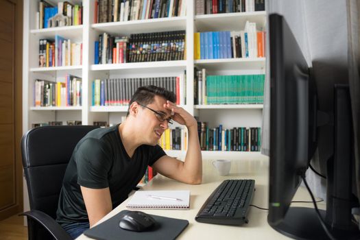 Man sitting in front of the computer in a shirt showing concern and despair because he does not understand something. Mid shot.