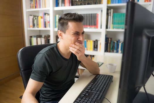 Man sitting in front of the computer in a shirt showing concern and despair because he does not understand something. Mid shot.