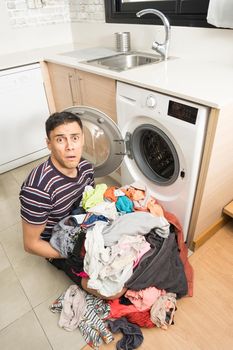 Man in casual clothes worried next to the washing machine, with a lot of dirty clothes on top. Full body.