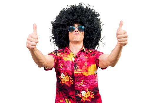 Positive man in vivid shirt with sunglasses and Afro wig pouting lips and gesturing thumbs up against white background