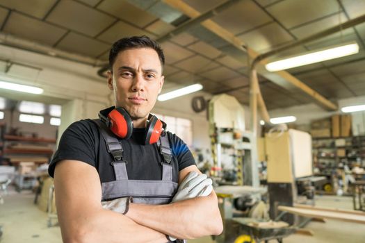 Worker standing with protective equipment looking at camera smiling in a factory. Mid shot.