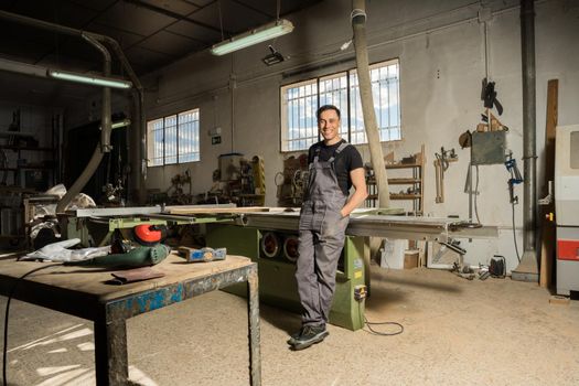 Worker standing looking at camera smiling in a factory. Long shot, full body.