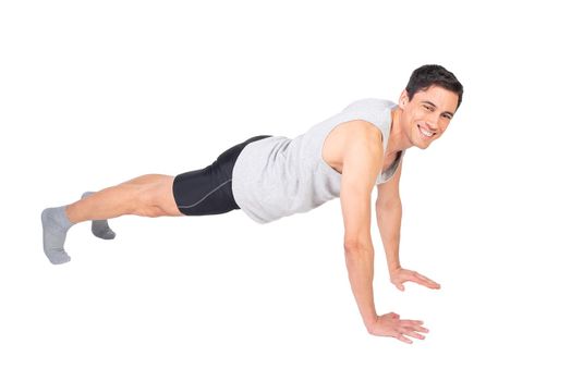 Full body of cheerful sportive male in sportswear looking at camera with smile while doing push ups isolated on white background