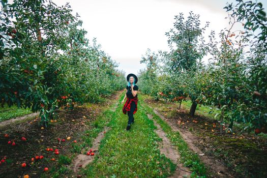 Pretty unusual woman with blue dyed hair walking alone between trees in apple garden at autumn season. Girl goes ahead away from camera. Organic, nature concept. High quality FullHD footage