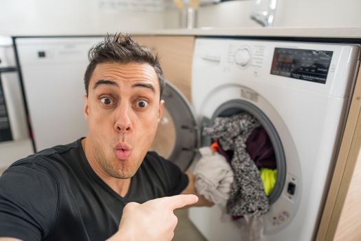 Man putting clothes in the washing machine, in the kitchen, worried because he has to wash a lot of clothes. Close up.