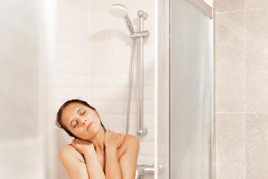 Front view of a relaxed woman with her eyes closed taking a shower in a hotel. Concept of Hotel.