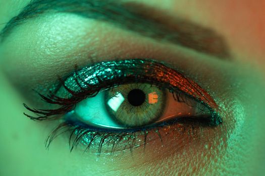 Extreme close up of female eye iris under neon light. Woman with beautiful makeup, glitter shadows and false lashes. Girls green eye. Nightlife, night club concept. High quality photo