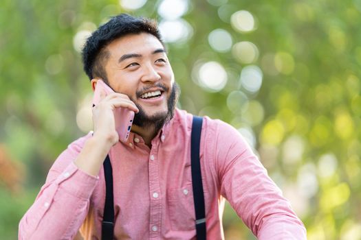 Portrait with focus on a happy chinese man with casual clothes talking to the mobile in a park