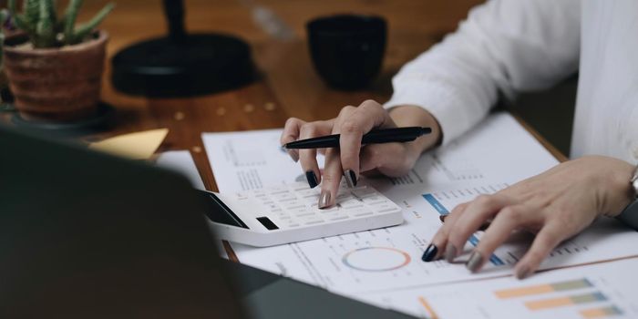 Close up Business woman using calculator and laptop for do math finance on wooden desk in office and business working background, tax, accounting, statistics and analytic research concept.