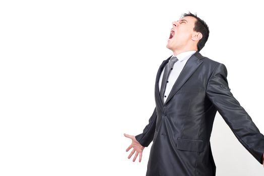 Frowning male office worker in formal suit spreading arms and yelling with closed eyes in studio against white background