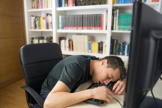 Seated man in black shirt asleep on the computer keyboard. Mid shot.