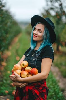 Blue haired woman picked up a lot of ripe red apple fruits from tree in green garden. Organic lifestyle, agriculture, gardener occupation. High quality FullHD footage