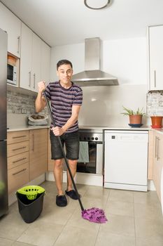 Smiling man wearing casual clothes and slippers mopping the kitchen floor. Full body.