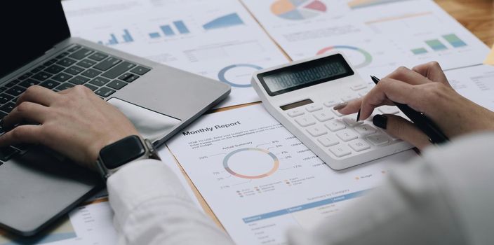 Close up Business woman using calculator and laptop for do math finance on wooden desk in office and business working background, tax, accounting, statistics and analytic research concept.