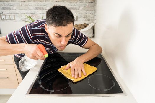 Man in casual clothes cleaning the induction hob in the kitchen with a cloth. Mid shot.