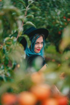 Pretty unusual woman with blue dyed hair walking alone between trees in apple garden at autumn season. Girl goes ahead away from camera. Organic, nature concept. High quality FullHD footage