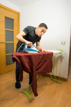 Man ironing a shirt at home with extreme care. Full body.