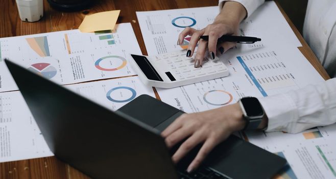 Close up Business woman using calculator and laptop for do math finance on wooden desk in office and business working background, tax, accounting, statistics and analytic research concept.