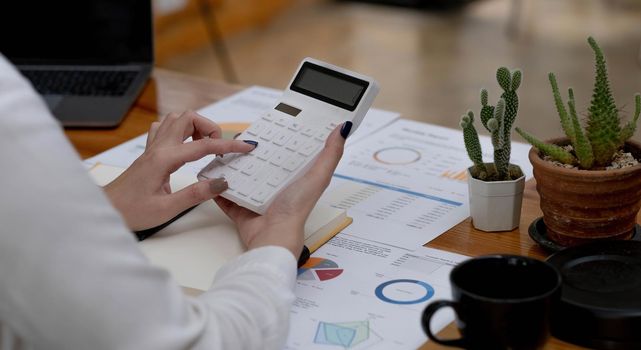 Close-up woman hand press calculator to calculate the company's financial results On the wooden table in the office and business work background, tax, accounting, statistics, and analytical research.