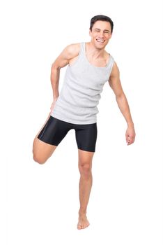 Full body of positive barefoot male in sportswear looking at camera while stretching quadriceps muscle isolated on white background in studio