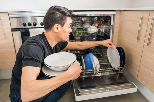 Man taking dishes out of the dishwasher in the kitchen. Close up.