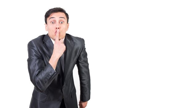 Quiet man in elegant suit covering mouth with finger and looking at camera while keeping silence isolated on white background