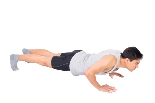 Full body side view of sportive male lowering body to ground while doing push ups exercise during fitness training isolated on white background