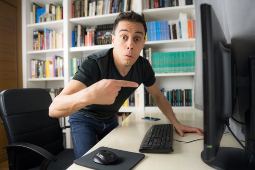 Seated man in black shirt looking at the computer screen very surprised. Mid shot.