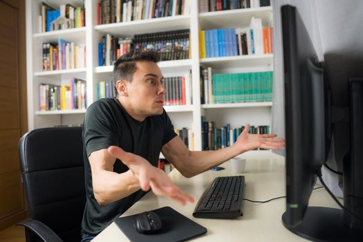 Man sitting in front of the computer in a shirt showing concern and despair because he does not understand something. Mid shot.