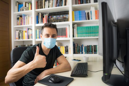 Man teleworking at home, sitting in front of the computer wearing a shirt and mask. Mid shot.