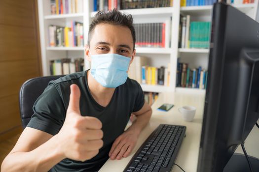Man teleworking at home, sitting in front of the computer wearing a shirt and mask. Mid shot.