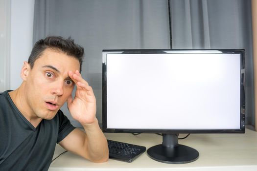 Surprised man in black shirt pointing at a computer screen announcing important news. Close up.