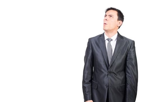 Mid shot of doubting male in elegant suit looking up with puzzled face while standing isolated on white background in studio