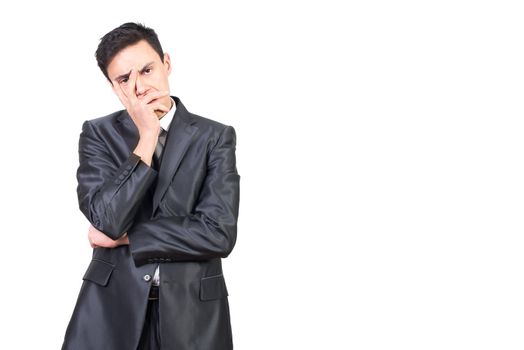 Calm tired young male entrepreneur with dark hair in elegant suit touching face and looking at camera against white background