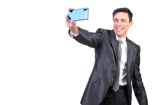 Happy male in formal suit smiling while taking self portrait on modern smartphone while standing isolated on white background in studio