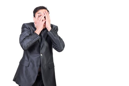 Scared young male entrepreneur with dark hair in formal outfit covering face and gazing at camera against white background