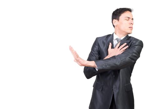 Harmed man in formal suit touching chest with hand while standing with closed eyes isolated on white background in studio
