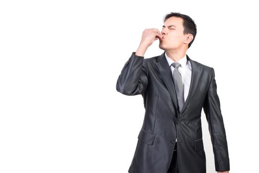 Adult male with dark hair and closed eyes wearing formal black suit kissing fingers while making delicious gesture against white background