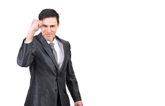 Self assured young male entrepreneur with dark hair in formal suit and tie showing fist and smiling at camera while standing against white background in studio