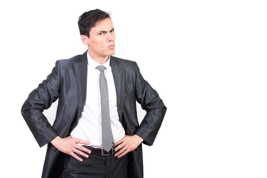 Handsome young man in elegant suit standing with hands on waist while looking angrily at camera on white background