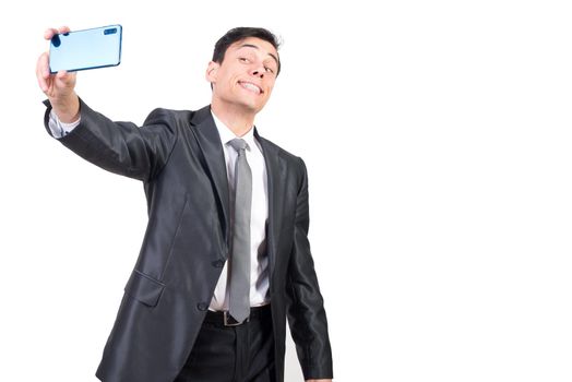 Cheerful male manager in formal suit smiling widely while taking self portrait on cellphone against white background