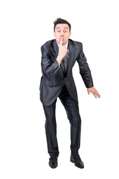 Full body of comic male entrepreneur touching lips and showing secret sign while standing against white background and looking at camera in studio