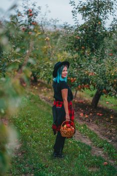 Pretty unusual woman with blue dyed hair walking alone between trees in apple garden at autumn season. Girl goes ahead away from camera. Organic, nature concept. High quality FullHD footage