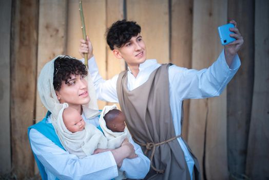 Nativity scene where two androgynous people taking selfie with a mobile while holding two babies