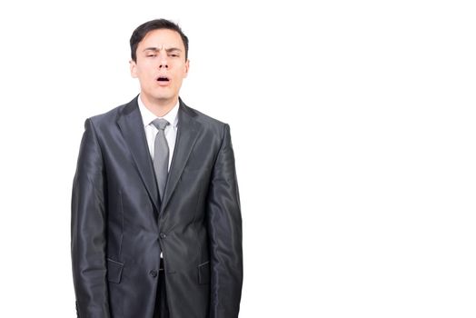 Tired man in elegant gray suit looking away with sleepy face while standing isolated on white background in light studio