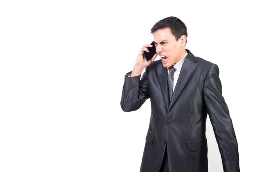 Serious angry businessman in formal suit talking on mobile phone while standing against white background in studio