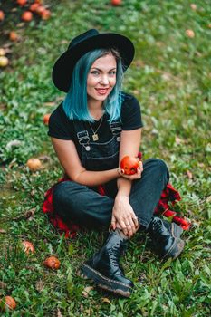 Blue haired woman picking up ripe red apple fruits in green garden. Organic lifestyle, agriculture, gardener occupation. High quality photo