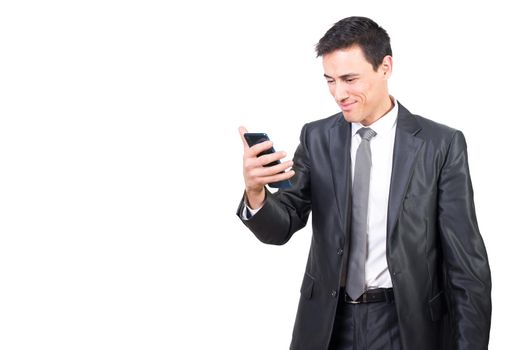 Positive male in elegant suit watching video on cellphone with smile while standing isolated on white background in light studio